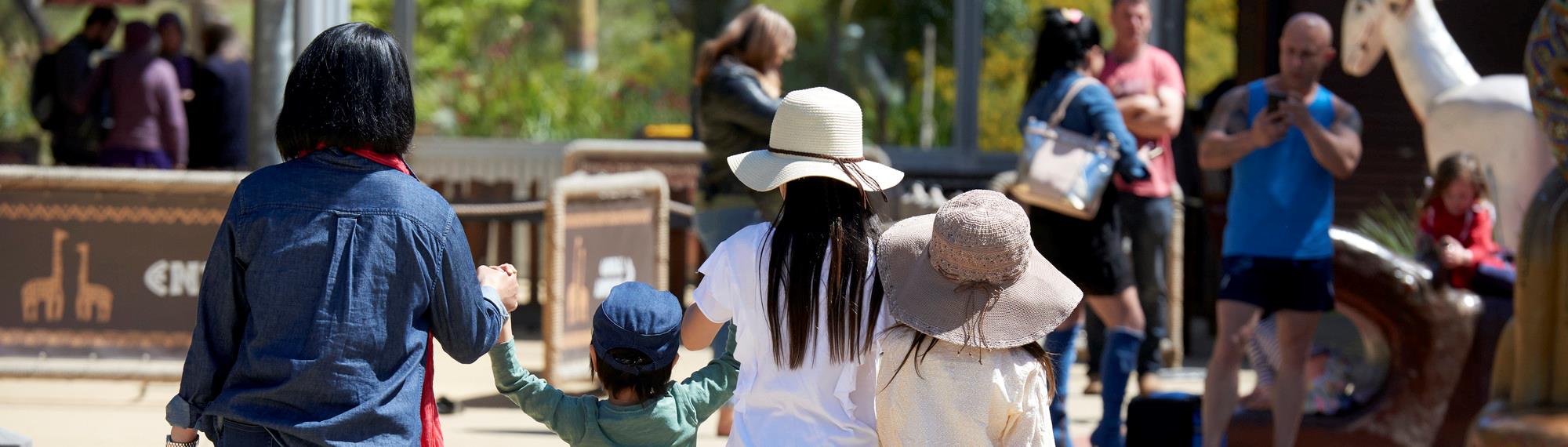 Family day out at Werribee Open Range Zoo. Visitors walking towards the entrance gate holding hands with young children.