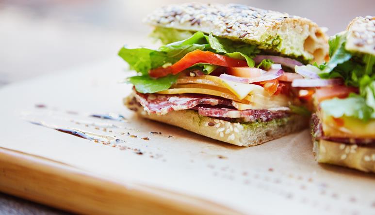 A cut sourdough sandwich on a platter, consisting of Beechwood ham, cheese, lettuce, tomato and red onion.