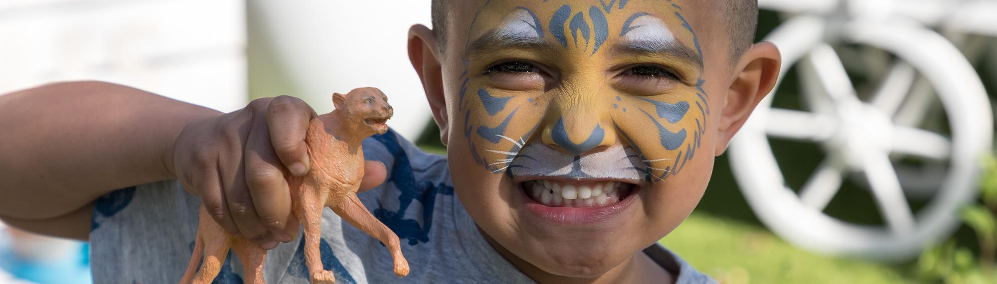 A young guest with Cheetah face-paint and holding a Cheetah figure, playfully snarling like a Cheetah.