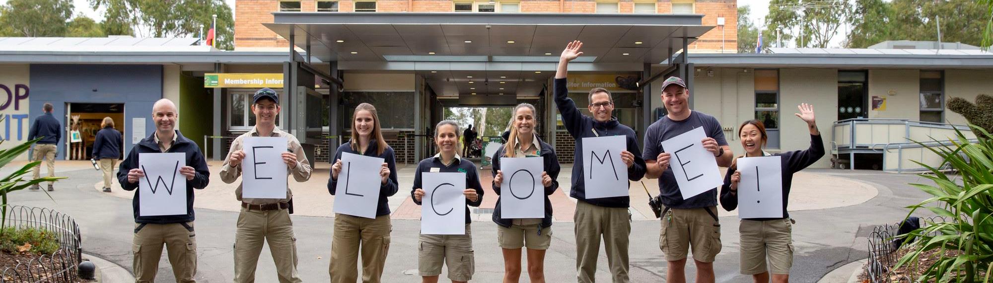 Eight zoo staff members standing in a line holding up letters spelling welcome!