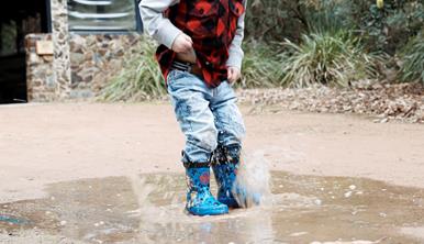 The lower half of a child hopping in a puddle.