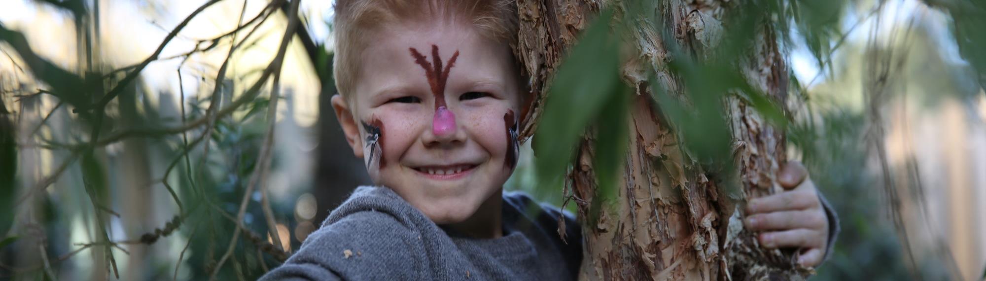 Smiling boy pretending to be a possum climbing a tree with possum face paint.