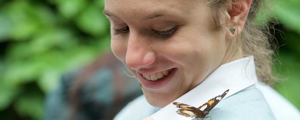 A female student looking down at a butterfly resting on her shoulder.