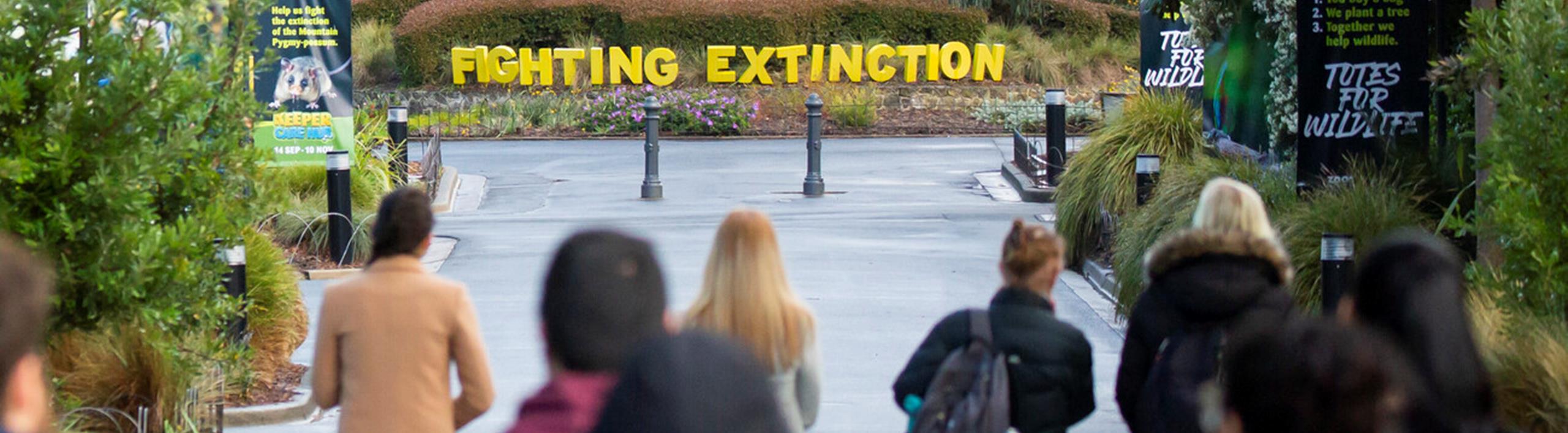 A group of people walking down a path, looking onto a sign saying Fighting Extinction, at Melbourne Zoo