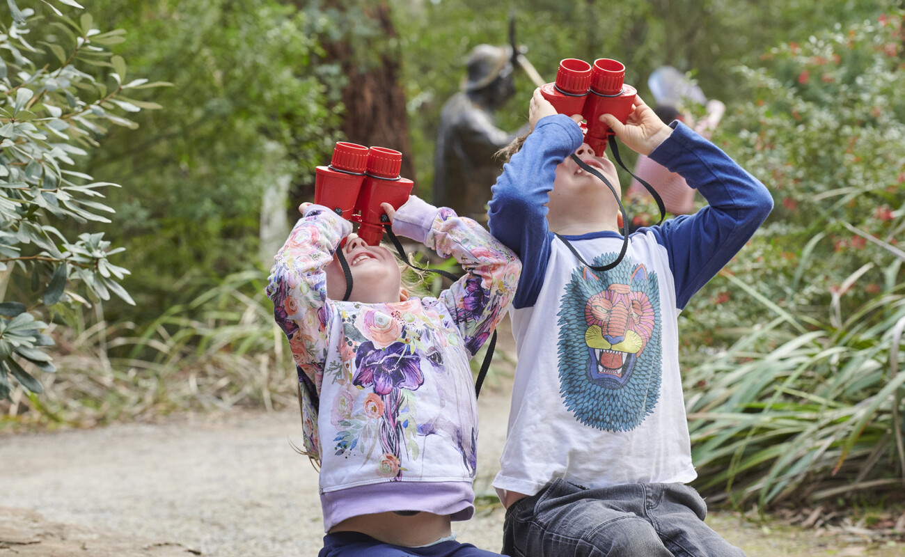 Two kinder kids look up to the sky through red binoculars
