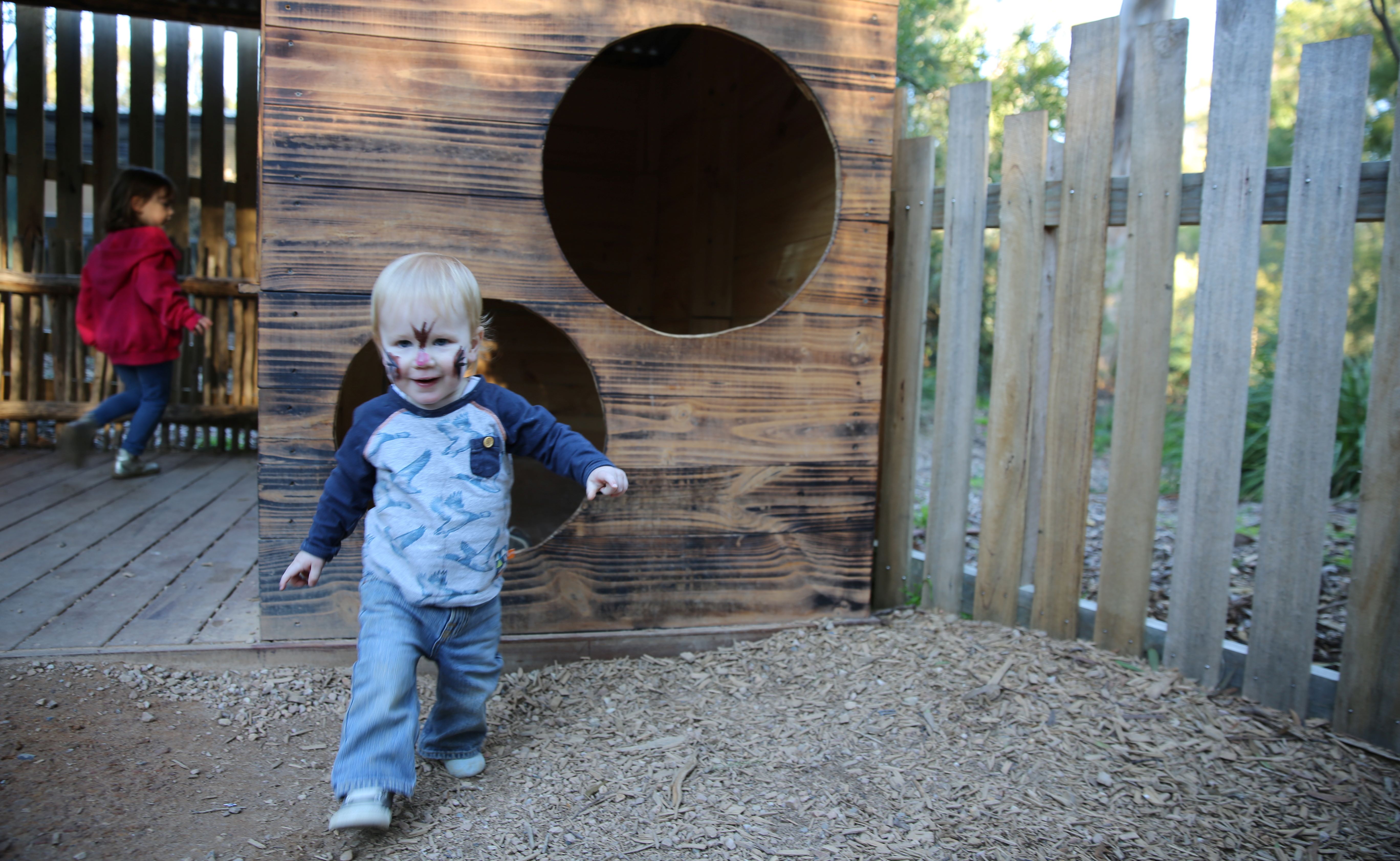 A boy walking towards the camera from the cubby house.