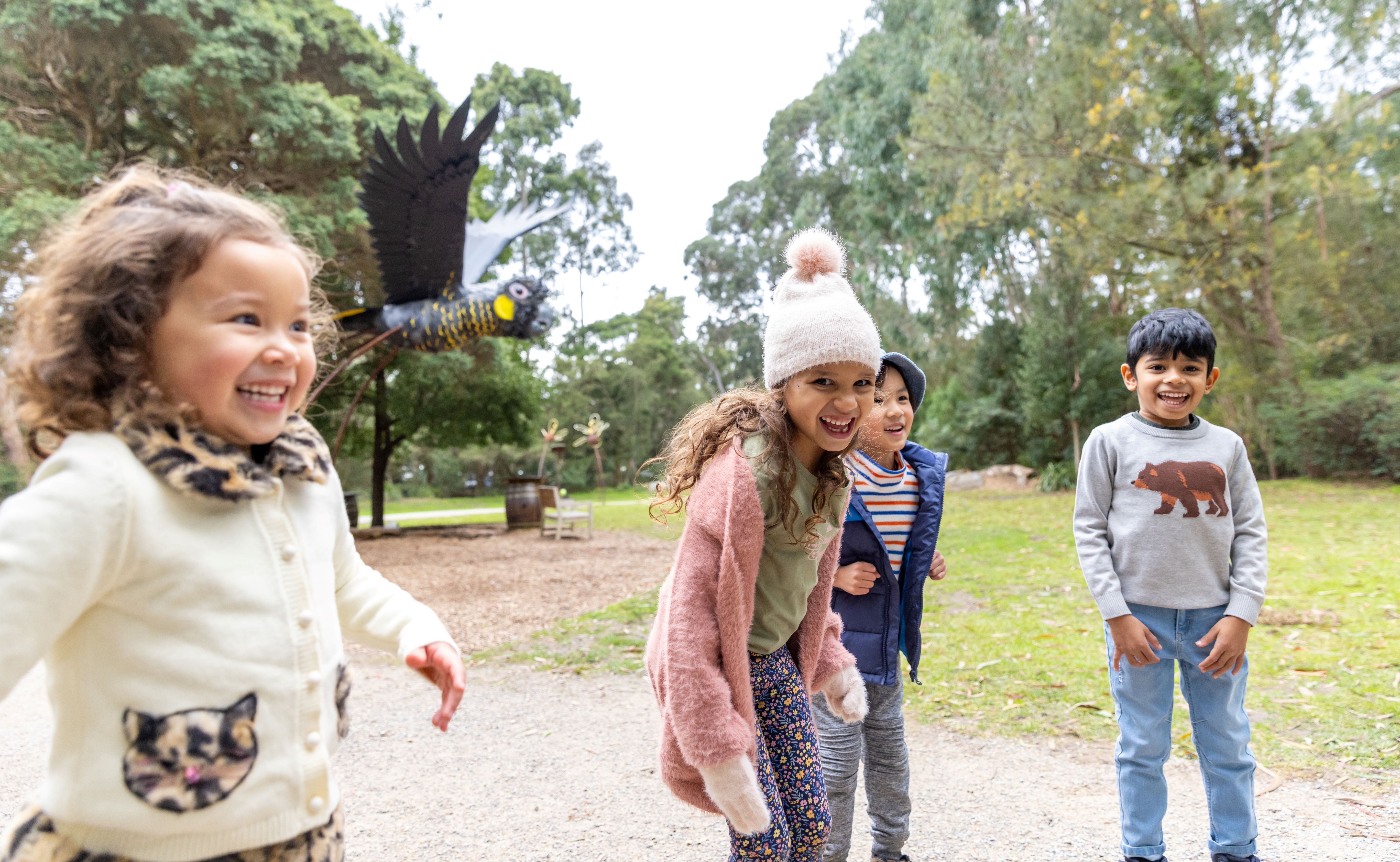 Four kids smiling with a giant Yellow-tailed Black Cockatoo at the back.